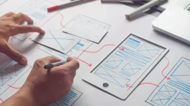 Pessoa criando design de interface em papel com laptop.