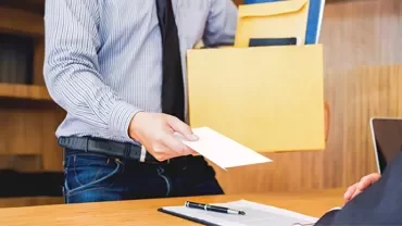 Pessoa entregando uma carta e pasta para alguém sentado em uma mesa.